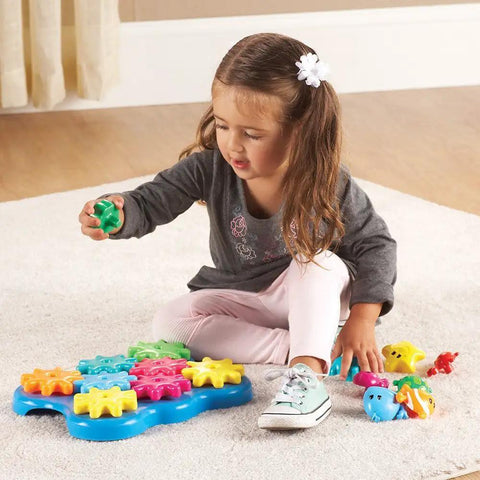Child playing with Ocean Wonders Build And Spin Gears Toy Set, a colorful STEM construction kit for toddlers, on a carpeted floor.