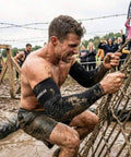 Man using Premium Padded Arm Sleeves with Compression Elbow Protection climbing muddy rope in obstacle race