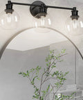 Three Light Industrial Vanity Fixture In Matte Black With Clear Glass Globes, in a modern rustic bathroom setting