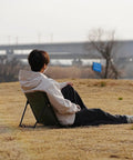 Person relaxing on Ultra Lightweight Outdoor Camping Backrest Chair With Carry Bag For Park Vibes And Beach Days.