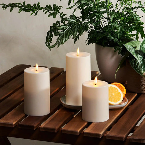 Waterproof Outdoor Flameless Pillar Candles 3 Pack In Ivory Resin on wooden patio table, LED flicker, 3x4, 3x5, 3x6 inches