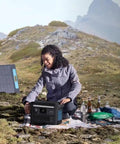 Two people setting up SOLIX C800X Portable Power Station with 100W solar panel on a mountain for outdoor camping.