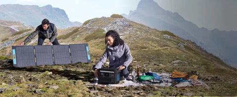 Two people setting up SOLIX C800X Portable Power Station with 100W solar panel on a mountain for outdoor camping.