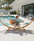 Wood Arc Hammock Stand With Double Hammock For Outdoor Use Natural Wooden Frame Supports Up To 330 Lbs 14 Feet Long Heavy Duty Chains And Carabiners Included Chill All Weather Lounging by a poolside.