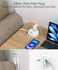 Gotta Love This Compact Travel Power Strip With Retractable Five Foot Cord And Seven Outlet Surge Protector Featuring Dual USB C And USB A Ports For Smooth Sailing On Cruise Vacations And Portable Jet Set Charging setup behind a sofa with flat plug, cable charging a smartphone and laptop.