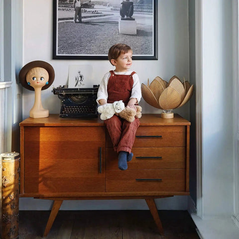 Child sitting on a wooden sideboard with decorative figurines and a typewriter, framed photo above.