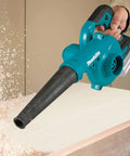 Heavy Hitter 18V Cordless Leaf Blower Featuring Variable Three Speed Control and 219 Mph Air Velocity blowing wood shavings off a surface.