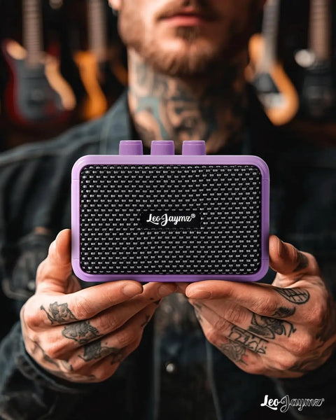 Man holding Compact 5W Guitar Amp For On The Go With Dual Speakers Bluetooth Wireless Connectivity Rechargeable Battery Clean And Overdrive Modes Gain Tone And Volume Controls Headphone Jack Ideal For Practice And Small Gigs Purple close-up