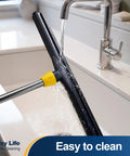 Big Time Heavy Duty Floor Squeegee Scrubber With Adjustable Telescopic Pole and Ergonomic Grip, rinsing under faucet.