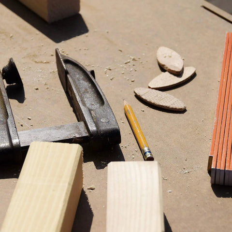100 Pcs Wood Joiner Biscuits Beech Wood Dowels Set in Three Sizes next to woodworking tools and pencil on a workbench.