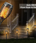 4 Pack Solar Torch Lights With Flickering Flame illuminating a garden path near a porch, showcasing outdoor waterproof stake lights.