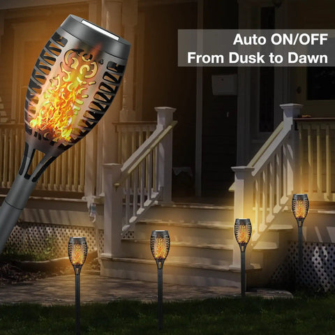 4 Pack Solar Torch Lights With Flickering Flame illuminating a garden path near a porch, showcasing outdoor waterproof stake lights.