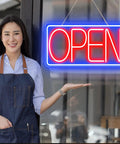 Person beside 16.5 Inch By 9 Inch LED Neon Open Sign For Business, Ultra Bright Plug In Light Up Sign With On Off Switch