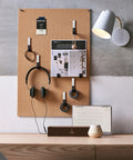 Pegboard organizer with headphones, photos, and cords under a wall lamp above a desk with calendar and decor.