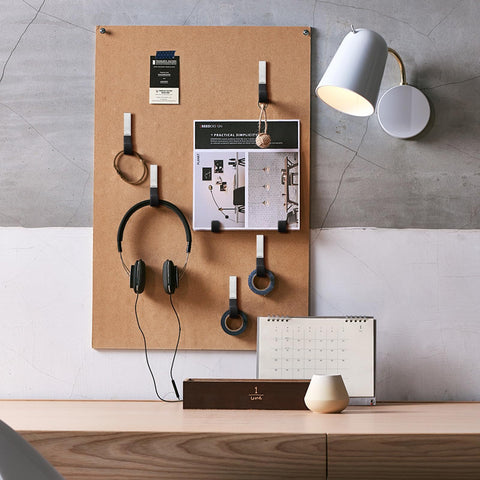 Pegboard organizer with headphones, photos, and cords under a wall lamp above a desk with calendar and decor.