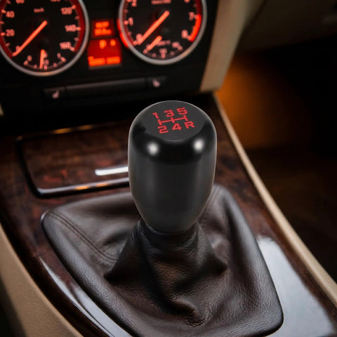 Upgrade Your Ride With This Sleek Kisa Angel 2 Piece Weighted Shift Knob Set For Manual Cars Featuring Ergonomic Grip, Anodized Finish, And Universal 8 10 12 Mm Adapter Kit For Smooth Gearing Action. Black aluminum manual shift knob with red 5-speed pattern in car interior