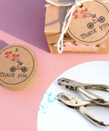Heavy Duty Handheld Paper Hole Punch for crafters with dual size options, shown with thank you tags and box on a pink background.