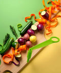 Green plastic handheld spiral slicer front view with cucumbers and colorful vegetables on a wooden cutting board.