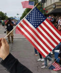 Person holding 12 Pack 8x12 Inch Handheld American Flags On Wooden Sticks With Kid Safe Spear Top For Memorial Day parade