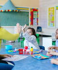 Children in a classroom playing with a Mini Firefighter Pretend Play Kit, including toy fire extinguishers and a ladder for role play.