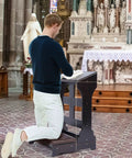 Man using Wooden Prayer Kneeler Bench With Cushion Pad For Home Or Church, Easy Assembly Kneeling Chair With Shelf, Sturdy Pine Wood Praying Stool 23W X 20D X 32H in a church setting