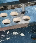 Woodworking hinge-boring drill bits set with self-centering hole saw in a blue jig, metal bit engaged in a hole.