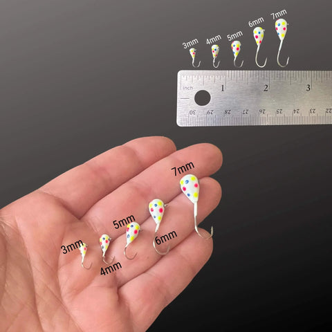 Hand holding colorful jigs with 3mm to 7mm sizes, ruler for scale, focusing on Tungsten Ice Jigs 6mm Variety Pack 10pcs With Long Shank Hooks For Ice Fishing And Panfish UV Glow Tear Shape Design Drops Fast Fewer Hangups Ultra Sensitive Tackle For Year Round Angling.