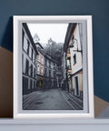 Framed black and white photo of a European street on a dark blue and beige background wall.