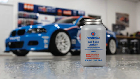 Front view of Permatex Anti-Seize Lubricant bottle with brush top, 8 oz, gray bottle with blue logo; blue car in workshop
