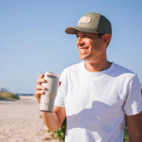 Smiling man holding a 20oz Ceramic Lined Travel Tumbler With Double Wall Vacuum Insulation and Secure Lid at the beach.
