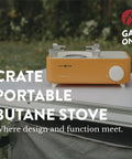 Butane Camp Stove For Hiking And Camping From The Crate Series on a table outdoors, orange, portable mini gas stove with spiral flame