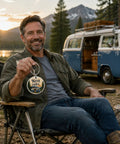 Man holding Camper Keychain For RV Lovers And Road Trip Fans by a blue van, mountain backdrop in camping setting
