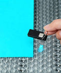 Magnetic honeycomb hold-down clamp on laser bed securing blue acrylic sheet; black rectangular magnet with metal patch.