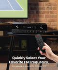 Person using remote with 600W Peak Two Channel Stereo Receiver With Bluetooth 5 3 Phono Optical Coaxial USB FM Mic In Aux RCA Input Karaoke Ready Home Theater Audio System With Remote near TV