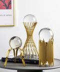 Decorative brass and glass orb sculptures on a table, including tall intertwined brass rods and geometric stands for home decor.