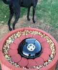 Red brick barbecue grill setup in garden with pebbles and black lid, dog visible in background.