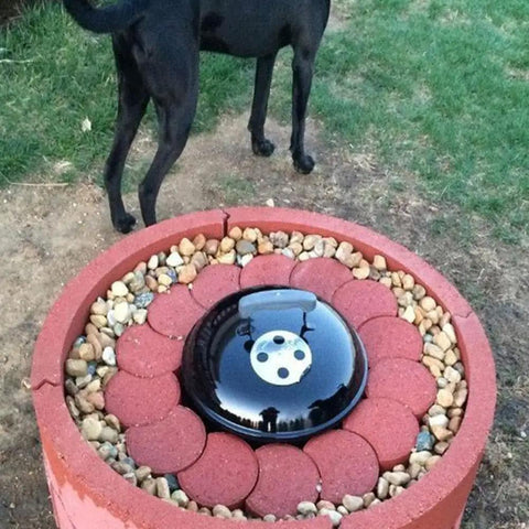 Red brick barbecue grill setup in garden with pebbles and black lid, dog visible in background.