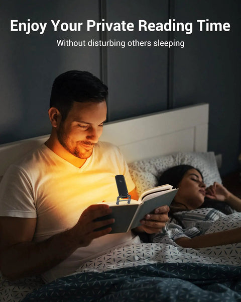 Man reading in bed using Amber Glow Clip On Book Light With 1800K Eye Care LED Rechargeable USB Reading Lamp, wife sleeping beside.