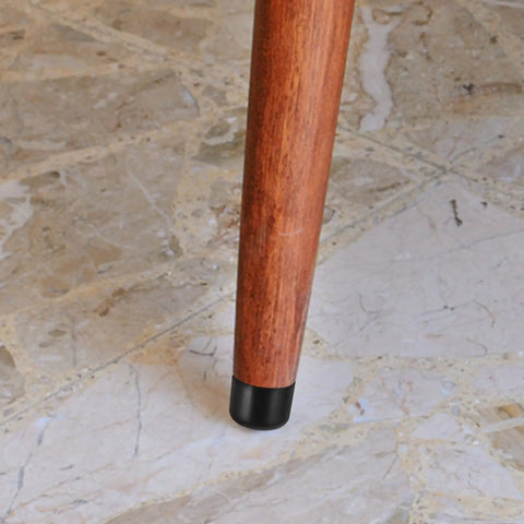 Close-up of wooden chair leg with black plastic cap on tile floor