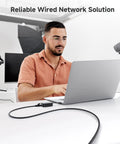 Man using laptop with 10Gbps Snagless Cat6 Ethernet Cable 25ft Slim Profile Patch Cord for reliable wired connection in office