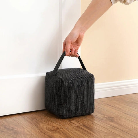 Heavy Duty Weighted Door Stopper With 4.4 Lb Internal Weight with handle, soft fabric, placed under white door on wood floor.