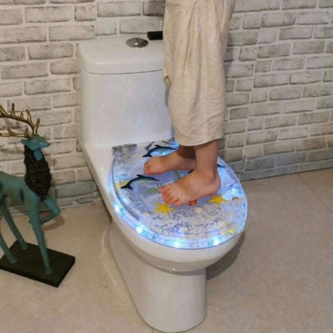 Child standing on Slick Transparent Dolphin Toilet Seat Featuring Smooth Glide Soft Close Lid Cover And Built In Led Night Light.