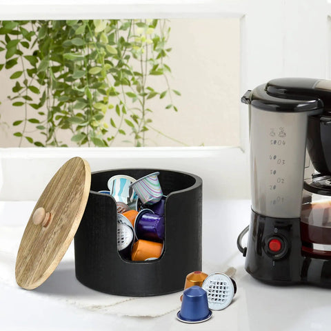 Wooden coffee filter holder and storage jar with lid beside a coffee maker, holding various coffee pods and filters