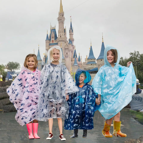 Children wearing fun design ponchos in front of castle, part of Disposable Rain Ponchos Family Pack Eight Pack With Hood For Adults And Kids