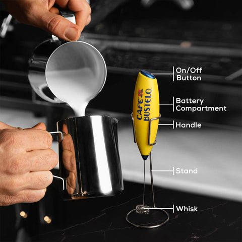 Electric Coffee Milk Frother Handheld Battery Operated Drink Mixer With Stainless Steel Whisk And Stand In Bold Yellow next to steaming milk pitcher