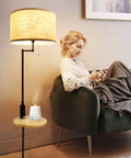 Woman relaxing on a sofa next to a modern floor lamp with a fabric shade and a small side table.