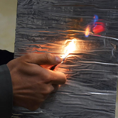 A hand holding a lighter against a Premium Synthetic Roof Underlayment Roll With Aluminum Foil Bitumen Tape for sealing.