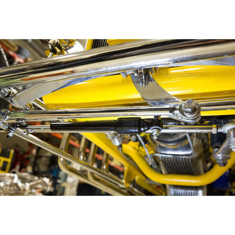 Close-up of chrome steering stabilizer for straight axle hot rods fits hairpin and four bar front suspensions reduces vibration and steering wobble includes seven eighths inch clamp kit for quick install and smoother handling installed under a vehicle.