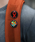 Two awareness pins on a red backpack, one with a red ribbon and the other with a heart made of colored puzzle pieces.