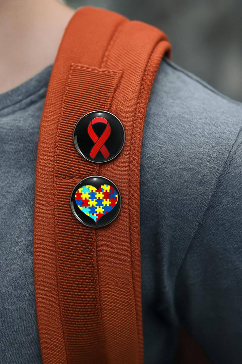 Two awareness pins on a red backpack, one with a red ribbon and the other with a heart made of colored puzzle pieces.